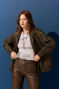 Genç ve güzel bir kadın, güz modasını ön plana çıkaran kahverengi deri bir elbiseyle rahatça poz veriyor..