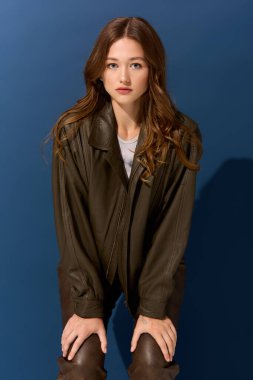 Genç bir kadın, sonbahar için ideal mavi stüdyo arkaplanı olan kahverengi deri bir elbise modelliyor..