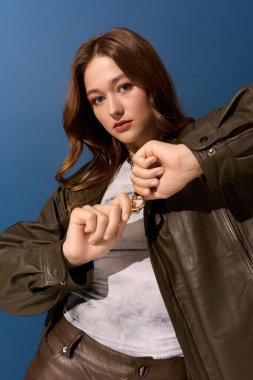 Genç bir kadın şık kahverengi bir deri elbiseyle poz veriyor. Mavi bir stüdyoda sonbahar atmosferini yakalıyor..