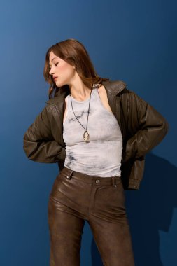 Kahverengi deri elbiseli genç bir kadın canlı mavi bir arka plana karşı poz veriyor, sonbaharı kucaklıyor..