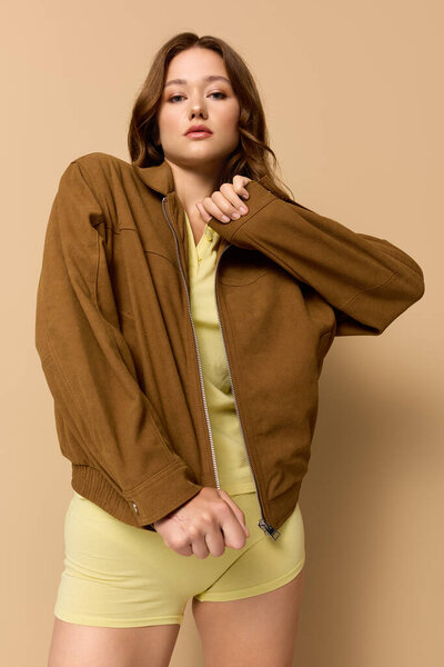 Young woman poses in a beige studio, showcasing her trendy autumn look in yellow.