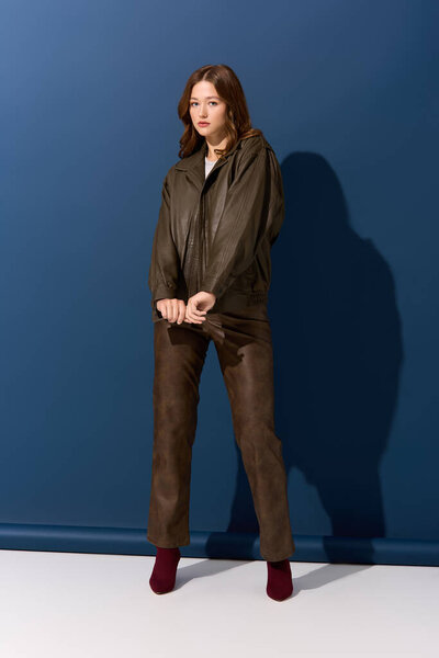 A stylish woman poses in a brown leather outfit against a bright blue autumn backdrop.