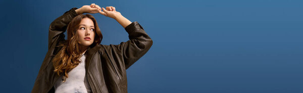 Красивая молодая женщина демонстрирует свою осеннюю моду в коричневой кожаной одежде в синей студии, баннер