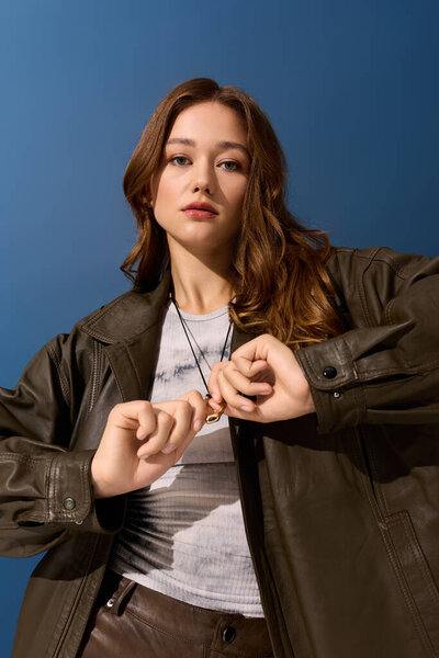 Молодая женщина уверенно позирует в шикарной коричневой кожаной одежде, принимая осенние модные тенденции.