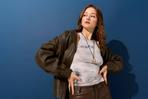 Красивая молодая женщина уверенно позирует в коричневой кожаной одежде на ярком синем фоне.