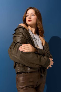 Genç ve güzel bir kadın, sonbahar modasını kahverengi deri kıyafetiyle sergileyerek poz veriyor..