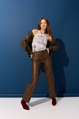 Genç bir kadın kahverengi deri bir elbise içinde mavi bir arka plana karşı poz veriyor, sonbahar için ideal..