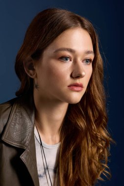 Kahverengi deri elbiseli güzel genç bir kadın zarif bir şekilde mavi bir arkaplanda poz veriyor..