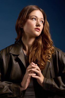 Güzel genç bir kadın zarif bir şekilde kahverengi deri bir elbise içinde canlı mavi bir arka plana karşı poz veriyor..