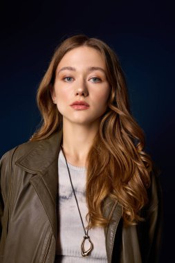 Güzel genç bir kadın kahverengi deri bir elbise içinde poz veriyor, mavi bir stüdyoda sonbahar trendlerini vurguluyor..