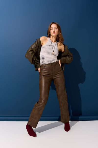 Молодая женщина позирует в коричневой кожаной одежде на синем фоне, идеально подходит для осени.