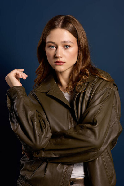 Молодая женщина позирует в коричневой кожаной одежде на ярком синем фоне.