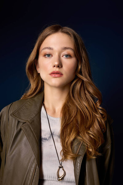 Pretty young woman poses in a brown leather outfit, highlighting autumn trends in a blue studio.