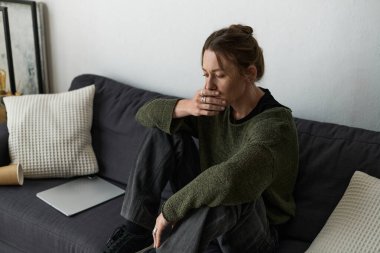 Evdeki sessiz bir anda, genç bir kadın koltukta otururken duygularını yansıtır..