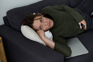 Genç bir kadın evindeki kanepede uzanıyor, üzüntü ve yalnızlık belirtileri gösteriyor..