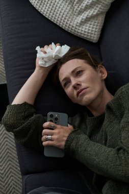 Genç bir kadın evinde bir kanepede dinleniyor, üzgün ve elinde bir mendille düşüncelere dalmış..