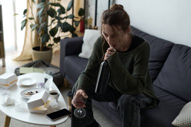 Genç bir kadın evinde üzgün ve yalnız bir şekilde kanepede oturuyor..