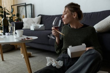 Genç bir kadın evinin zemininde oturmuş şarabın tadını çıkarıyor ve düşüncelerini düşünüyor..