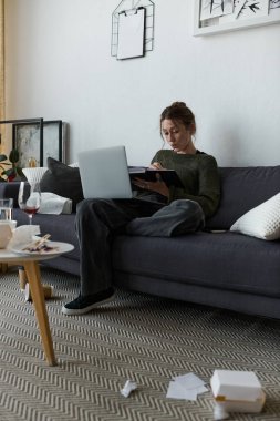 Genç bir kadın kanepede tek başına oturur, çabalarını ve duygularını yansıtır..