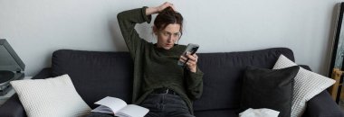 Evindeki bir kanepede oturan genç bir kadın telefonuna bakarken huzursuz görünüyor..