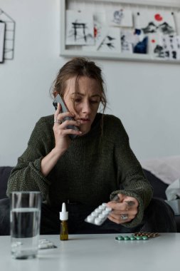 Genç bir kadın telefonda düşünceli ve üzgün bir şekilde kanepede oturuyor..