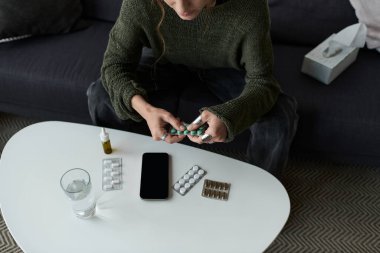 Genç kadın kanepede oturuyor, evde ilaçlarını alırken bunalmış hissediyor..