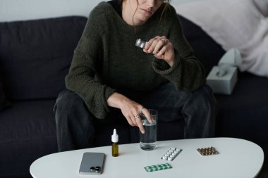 Kanepede oturan genç bir kadın elindeki su ve ilaçla depresyonu yansıtır..