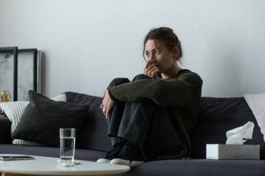 Rahat bir evde, genç bir kadın bir kanepeye kıvrılmış, düşüncelere dalmış ve keyifsiz bir şekilde oturuyor..