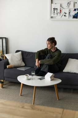 Genç bir kadın, sessiz bir öğleden sonra yalnız başına koltuğunda oturup üzüntüsünü yansıtıyor..