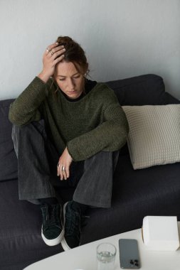 Genç bir kadın kanepede oturuyor, evinde yalnız başına duygularını ifade ediyor..
