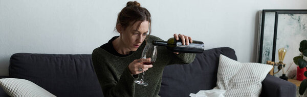 В своей уютной гостиной молодая женщина молча борется с депрессией, наливая вино в бокал..