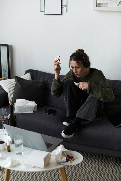 A young woman sits on a couch with headphones, deep in thought, surrounded by takeaway leftovers.