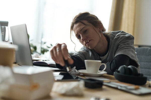 A young woman sits at home, feeling overwhelmed, surrounded by empty cups and clutter.