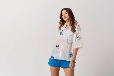 Şık bir genç kadın kendine güvenerek poz veriyor, şık yaz kıyafetlerini parlak bir mekanda sergiliyor..