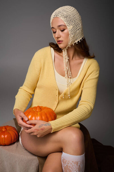 A woman in a yellow cardigan hugs a pumpkin, radiating autumn vibes with her smile.