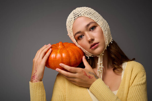 Chic young woman showcases her style while holding a vibrant pumpkin.