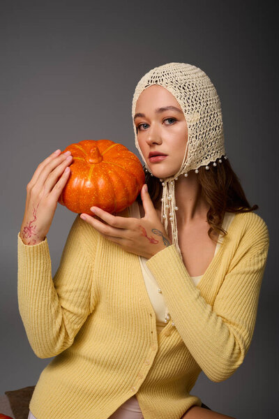 Stylish young woman poses with a pumpkin, showcasing a blend of fashion and seasonal charm.