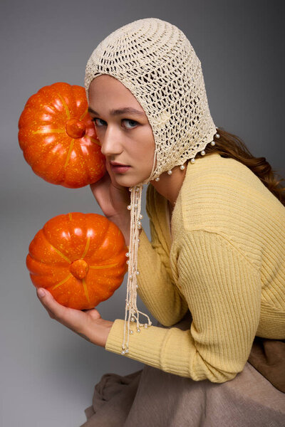 Young woman in chic attire holds bright pumpkins, striking a unique pose that captures autumn vibes.