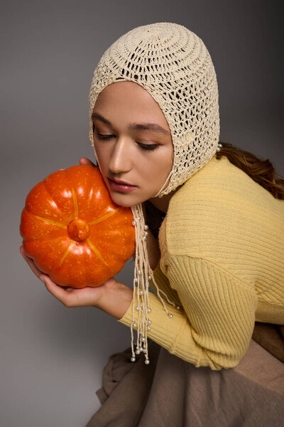 Beautiful young woman showcases her stylish outfit while tenderly holding an orange pumpkin.
