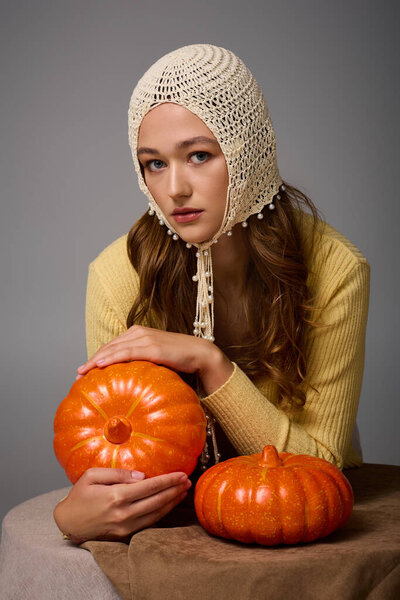 Fashionable young woman sits gracefully, showcasing pumpkins, blending style and seasonal charm.