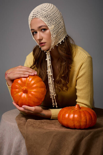 A young beautiful woman poses with pumpkins, embodying style and warmth in a fall atmosphere.
