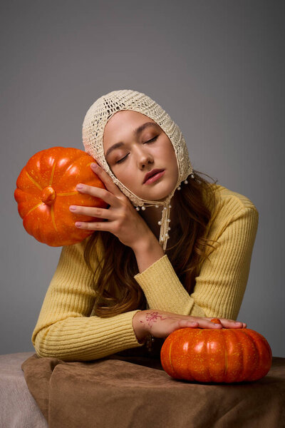 A fashionable young woman sits quietly, embracing pumpkins and enjoying the autumn vibe.