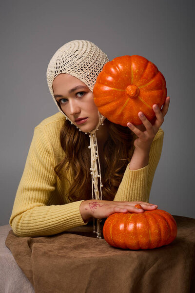 Chic woman in a knitted hat and sweater showcases pumpkins, fully embracing autumn.