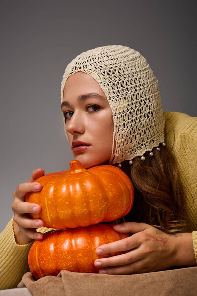 Charming young woman in stylish attire enjoys a creative moment with pumpkins in a seasonal setup.