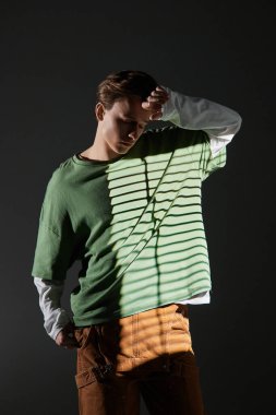 Kıyafetlerinde benzersiz ışık desenleri olan şık kıyafetli genç adam dramatik bir şekilde poz veriyor..