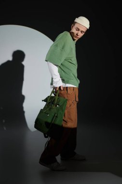 Modaya uygun bir genç, gençlik kültürü ve tarzını harmanlayan yeşil bir çantayla güven içinde poz veriyor..