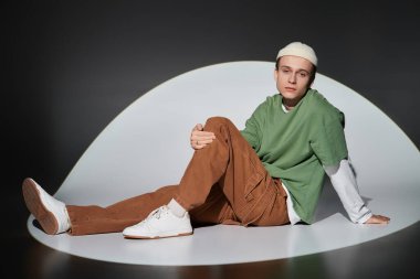 Moda kıyafetleri giymiş gençler kıvrımlı bir yüzeyde şık bir şekilde uzanır, kentsel gençlik kültürünü somutlaştırır..