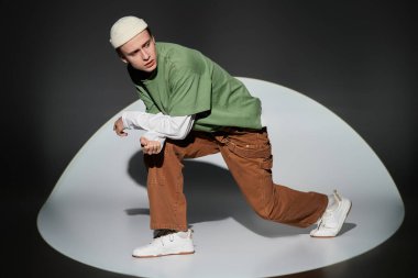 Moda kıyafeti giymiş genç adam dinamik bir poz verirken kendine güvenini ve tarzını sergiliyor..