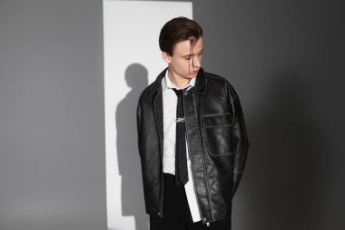 Genç bir adam, kendine has tarzını deri ceketi ve kapalı mekanda kendine güvenen pozuyla sergiliyor..