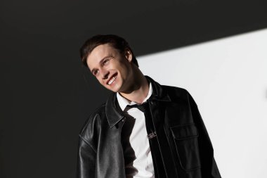 Kendine güveni tam bir genç, şık bir kıyafetle bir şehir arkaplanına gülümsüyor..